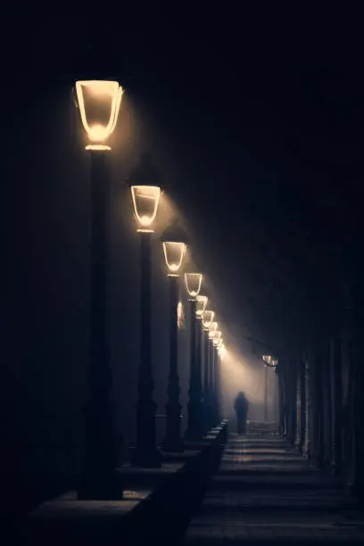 person walking on dark street illuminated with streetlamps