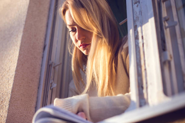 istock Blonde woman reading book at home 664091154