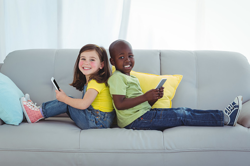 Smiling girl and boy using mobile phones on the couch