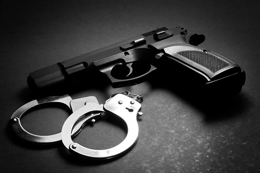 Handgun with handcuffs over dark background