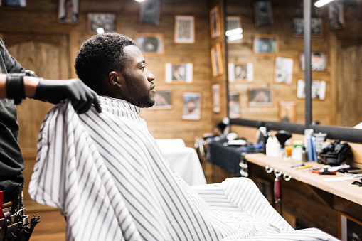 African guy sitting in barbershop covered by napkin