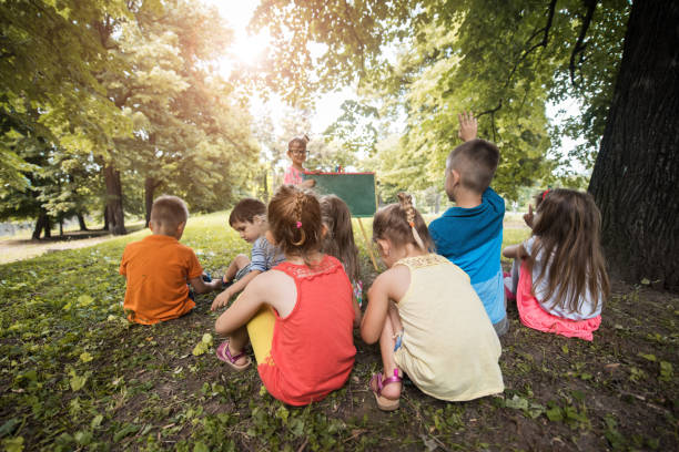istock Back view of kids learning from their friend in nature. 664152178