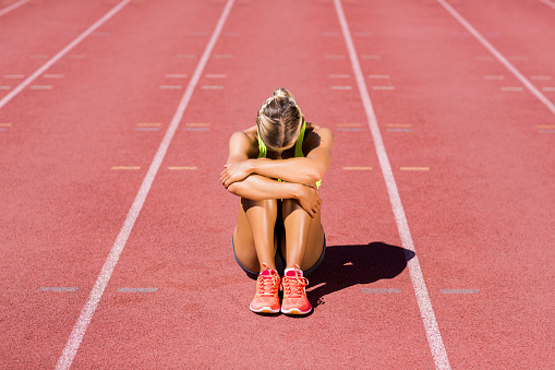 Upset female athlete sitting on running track on a sunny day
