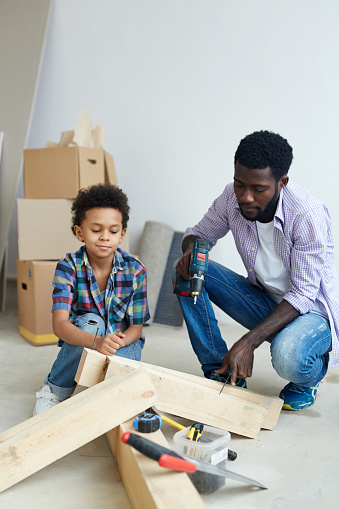 Young man working with power-tool with son near by