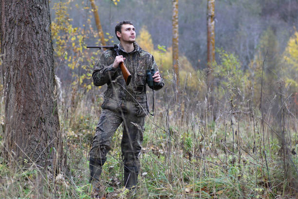 istock Man in camouflage and with guns in a forest belt on a spring hun 664178406