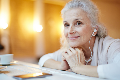 Contemporary senior female with earphones listening to music at leisure