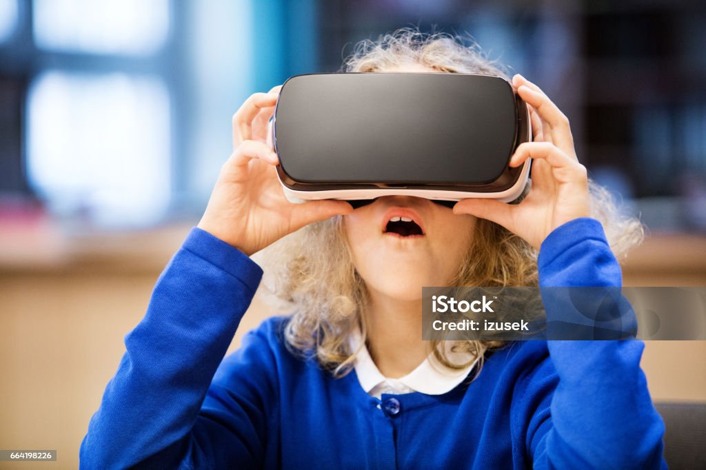 Cute girl using virtual reality goggle at school Excited girl wearing school uniform, using virtual reality goggle at school Virtual Reality Simulator Stock Photo