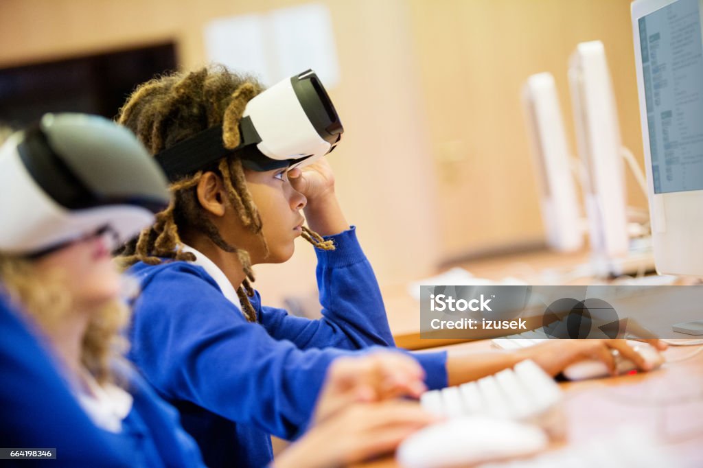 Mixed race group of students using virtual reality goggles Mixed race group of excited students sitting in a computer lab at school and using virtual reality goggles. High School Stock Photo