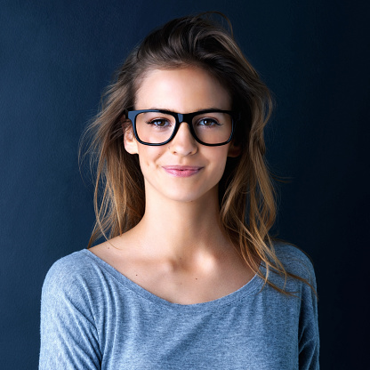 Studio portrait of a cute teenage girl in glasses posing against a dark background