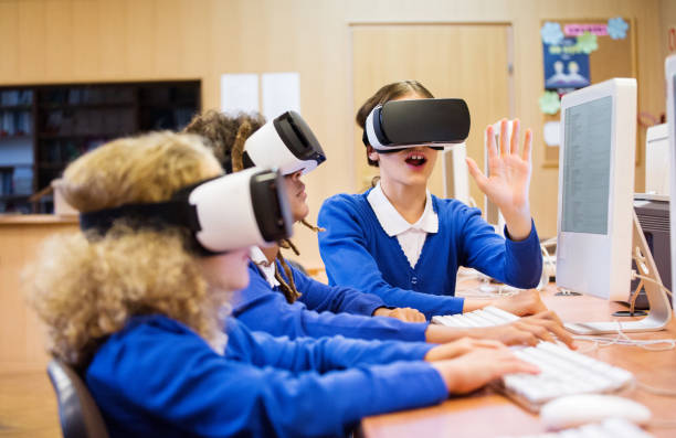 Mixed race group of students using virtual reality goggles Mixed race group of excited students sitting in a computer lab at school and using virtual reality goggles. high school high school student science multi ethnic group stock pictures, royalty-free photos & images