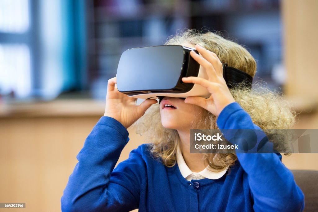 Cute girl using virtual reality goggle at school Cute girl wearing school uniform using virtual reality goggle at school. Virtual Reality Simulator Stock Photo