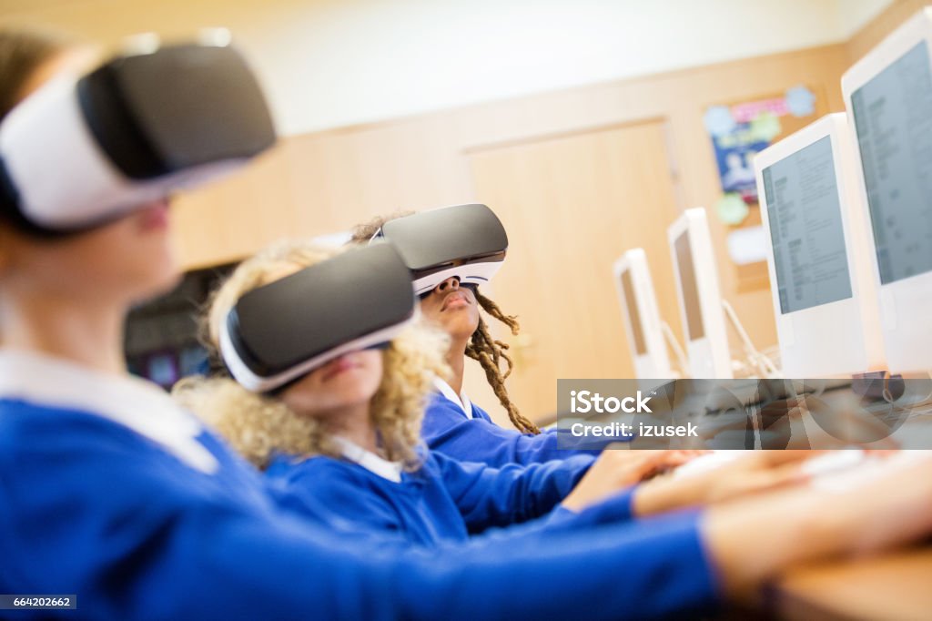 Mixed race group of students using virtual reality goggles Mixed race group of excited students sitting in a computer lab at school and using virtual reality goggles. Three Dimensional Stock Photo
