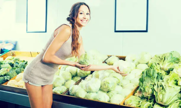 Glad female customer holding fresh cabbage-head on market
