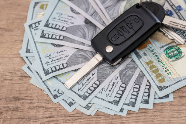 Car key lying on US 100 dollar bills on wooden desk.
