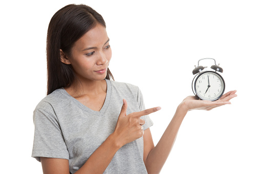 Young Asian woman point to a clock  isolated on white background.