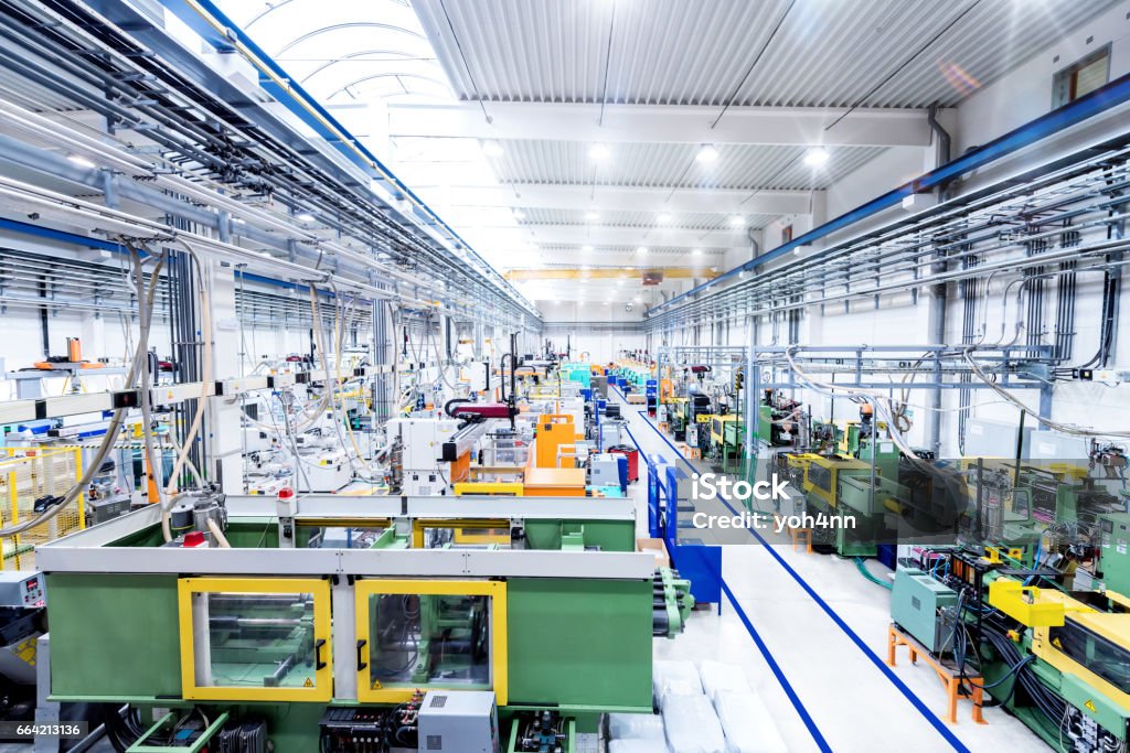 Industrial new factory & modern machines Horizontal color image of futuristic factory. Industrial aisle surrounded by modern machines which having busy robotic arms with molding shapes and producing plastic pieces for variety of industry. Labor intensive production line with manufacturing equipment. Machinery Stock Photo