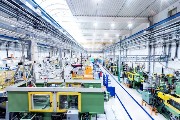 Horizontal color image of futuristic factory. Industrial aisle surrounded by modern machines which having busy robotic arms with molding shapes and producing plastic pieces for variety of industry. Labor intensive production line with manufacturing equipment.