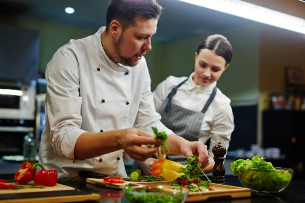 Cooking together Chef consulting his trainee while cooking salad chef stock pictures, royalty-free photos & images