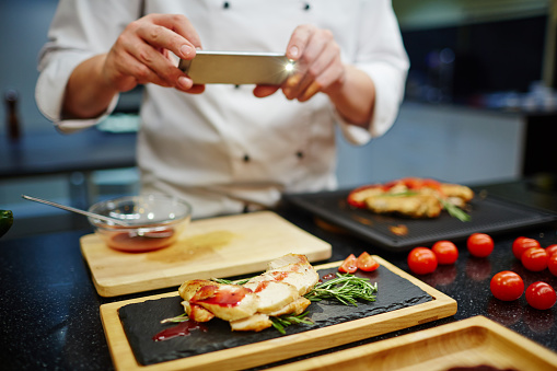 Chef photographing roasted chicken steak dressed by tomato sauce