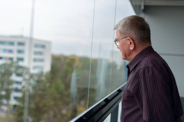 istock Old man thinking while looking outside glass window of modern building 664238226