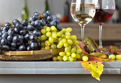 Blue Isabella grapes bunch , Green grapes bunch with the autumn leaves and ripe pomegranate on kitchen table . Glasses with red wine and white wine .