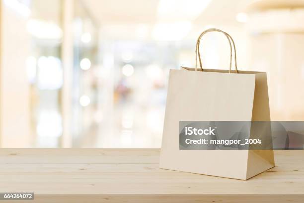 Brown Paper Shopping Bag On Wood Table Over Blurred Store Background Business Template Retail Sale Stock Photo - Download Image Now