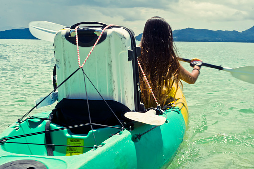 Close up rear shot of a young Asian woman in a bikini exploring remote tropical islands on her kayak with her beloved white suitcase strapped in behind her