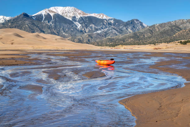 whitewater kayak in shallow water and sand dunes whitewater kayak in shallow waters of Medano Creek with Great Sand Dunes and Sangre de Cristo Mountains in background great sand dunes national park stock pictures, royalty-free photos & images