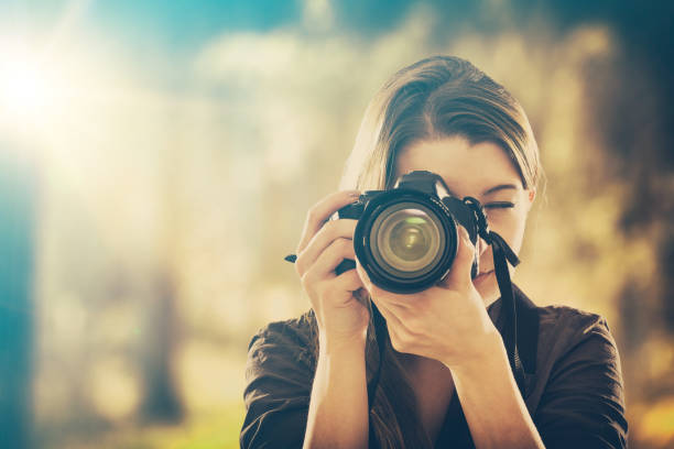Portrait of a photographer covering her face with camera. photographer camera dslr photo person portrait photographing girl joy make photography taking concept - stock image sepia toned photos stock pictures, royalty-free photos & images