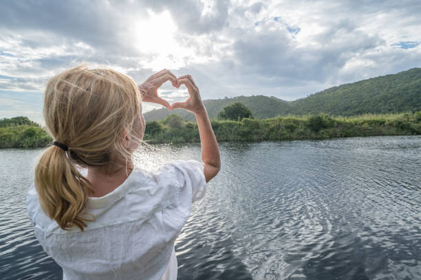istock Young female by the river making heart shape finger frame 664305312