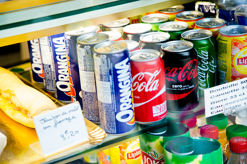 Paris, France - October 08, 2015: Several soft drink cans in a shop window. We can see various cans of Orangina, Coca Cola classic, Coca Cola Zero, Coca Cola Life, Lipton, and Jocker