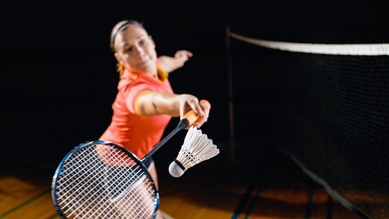 Young woman stretching to hit shuttlecock in badminton court.