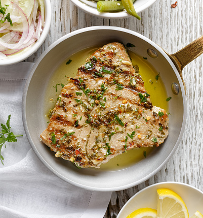 Grilled tuna steak in herb and lemon marinade served on a rustic pan, top view