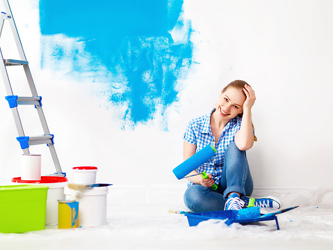 Repair in the apartment. Happy woman paints the wall with blue paint