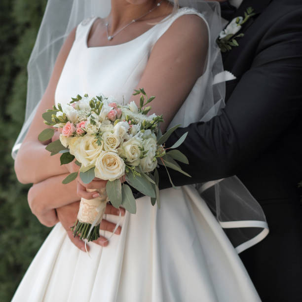 istock bride holds a wedding bouquet in hands, the groom hugs her from behind 664406404