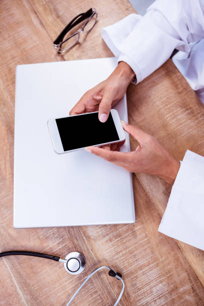 istock Doctor using smartphone on wooden desk 664406674