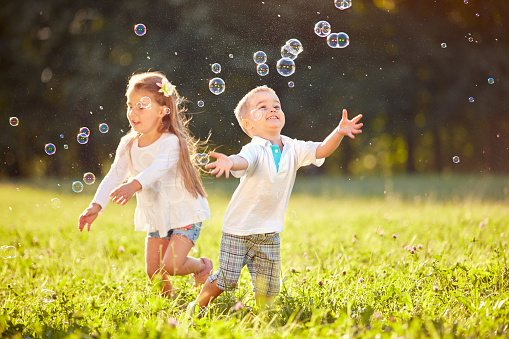 Cheerful children run and chase bubbles in nature