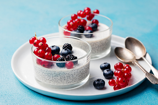 Chia seed pudding, cheesecake, custard dessert with fresh berries in a glass bowl on white plate. Copy space