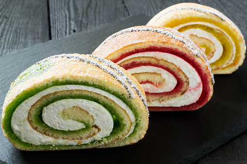 Delicious cake roll with fruit marmalade (kiwi, strawberry, lemon) and marshmallow. Sliced rolls on a slate plate. Tasty fruit dessert. Selective focus