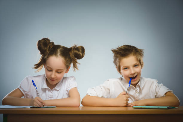 Happy girl and boy sitting at desk on gray background. school concept stock photo