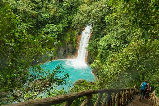 Two young woman going down a wooden stairs at the waterfall of river Celeste. River has beautiful turquoise color in the rain forest. River Celeste in Tenorio Volcano National Park, Costa Rica.