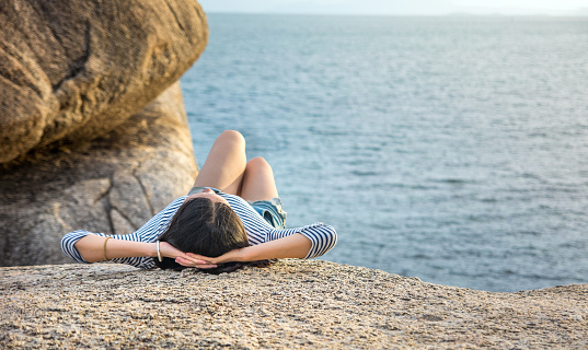 Girl lying on the cliff above seaside at sunset time