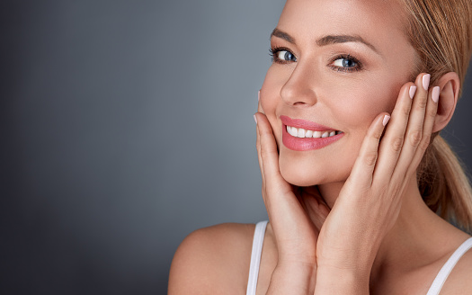 Smiling woman enjoying in her healthy skin, middle aged lady touching her face