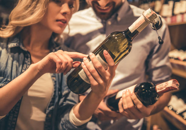 Couple at the supermarket Beautiful young couple is talking and smiling while choosing wine at the supermarket alcohol shop stock pictures, royalty-free photos & images