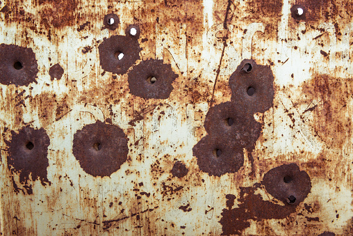 Rusty small calibre bullet holes in a rusty piece of metal once painted white.