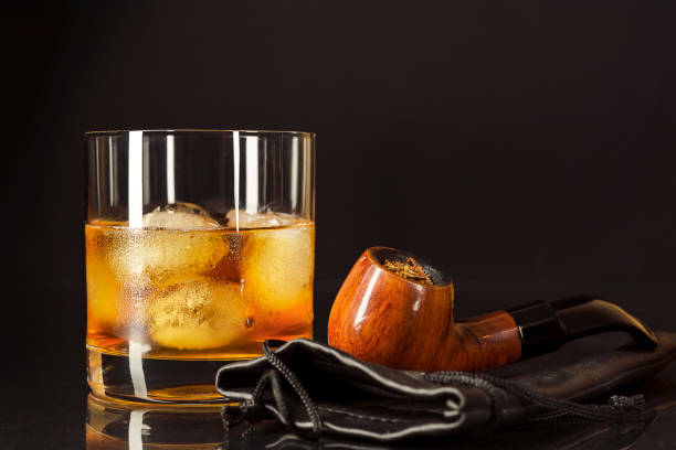 Scotch drink glass and smoking pipe on black background