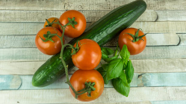 istock Red tomatoes and cucumbers with basil on a wooden table 664501312