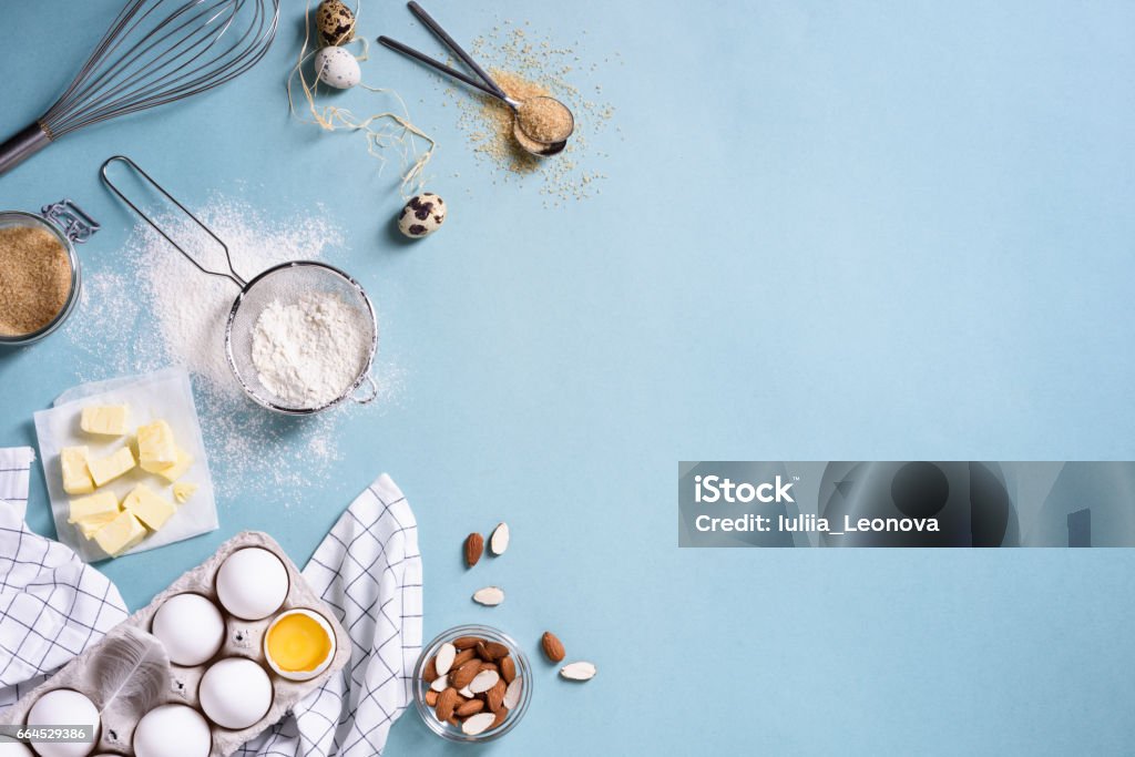 Healthy baking ingredients - flour, almond nuts, butter, eggs, biscuits over a blue table. Healthy baking ingredients - flour, almond nuts, butter, eggs, biscuits over a blue table background. Bakery background frame. Top view, copy space. Flour Stock Photo