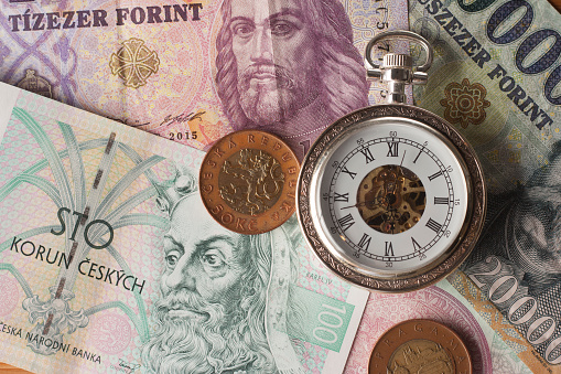 Czech and hungarian currency and vintage clock on wooden background