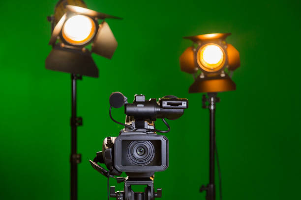 una cámara de vídeo y un foco de luz con una lente de fresnel sobre un fondo verde. rodaje en el interior. la clave de croma - fresnel fotografías e imágenes de stock